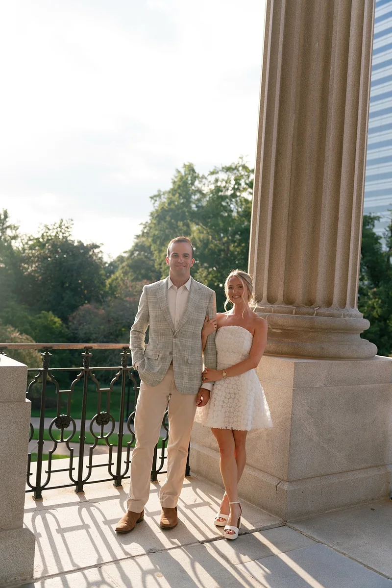 Ellie and Marcus arm in arm beside a State House column