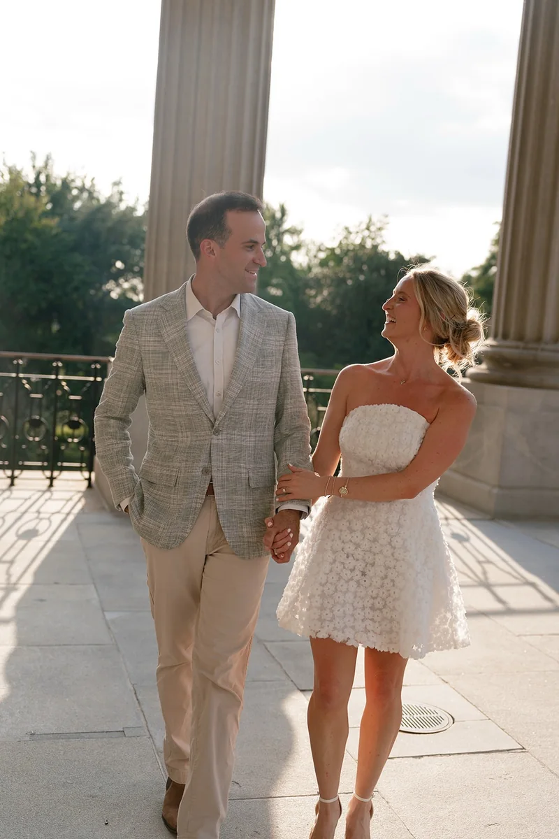 Ellie and Marcus walking hand in hand along the State House portico, Ellie laughing